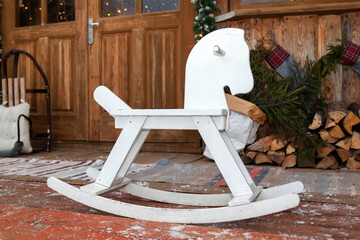 Yard of house is decorated for christmas. Winter porch of house is decorated with fir trees, wooden rocking horse