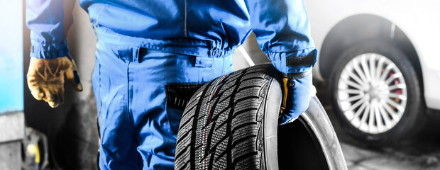 Mechanic holding tire with copy space for text repair service center, blurred background, - obrazy, fototapety, plakaty