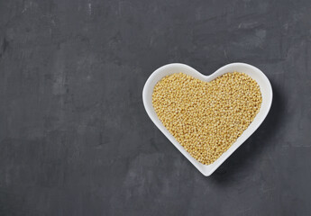 Raw pasta ptitim on heart-shaped plate on dark gray table. Top view.