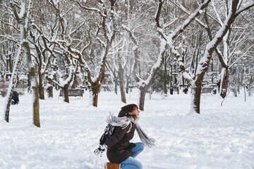 Fototapeta na wymiar Happy young woman playing with snow in a snow-covered winter park. Girl enjoying snowy winter, frosty day. Walk in winter forest