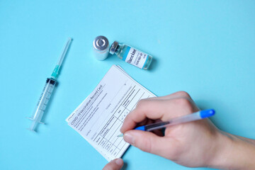 doctor's hand filling out vaccination passport. Immune passport or certificate for travel concept. 2019-ncov Covid-19 Corona Virus drug vaccine vial medicine bottles syringe injection. SARS-CoV-2