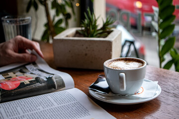 Hand of a person leafing through the newspapers or a magazine, with a cup of coffee in front of a cafe window. 