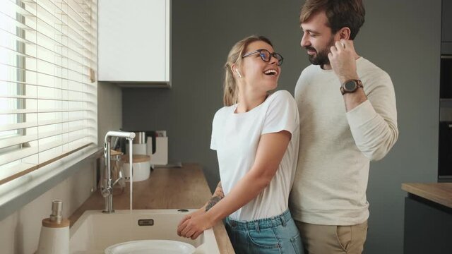 A happy man is dancing with his girlfriend while washing the dishes at home