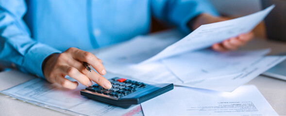 Detail on business person fingers counting on a calculator and reading a  contract or bill on official paper. Contract management, good business deal.