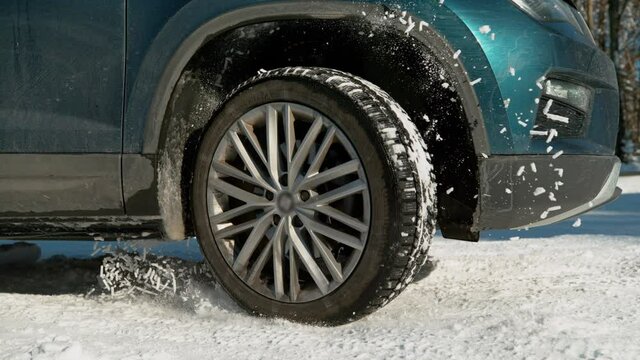 SLOW MOTION, LOW ANGLE, CLOSE UP, DOF: SUV's wheels spin in place and spew up pieces of white snow as it attempts to gain traction on the slippery road. Snow flies up from a blue car's spinning wheel.