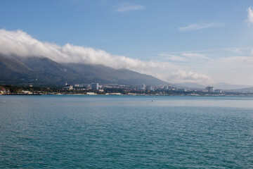 Fototapeta premium A white cloud lies on a mountain against the background of the sea