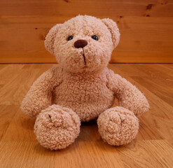 A cute stuffed teddy bear. Softly smiling kindly. Close up and isolated against a wooden background.