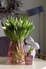A bouquet of white tulips in a purple glass vase. Large and small glass vases with tulips on a blurry background.