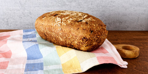 Freshly baked spelt bread on colorful tea towel and wooden board. Homemade fresh bread loaf.