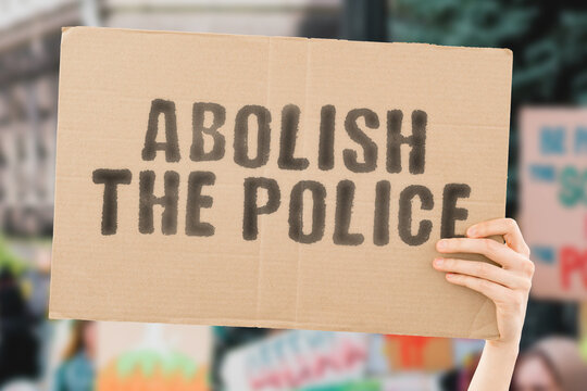 The phrase " Abolish the police " on a banner in men's hand with blurred background. Dangerous. Aggressive. Danger. Conflict. Behaviour. Battle. Fight. Illegal. Angry
