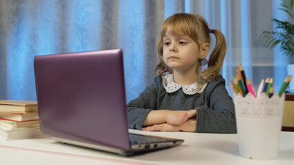 Child girl doing school homework, writes in notebook, using laptop computer at home. Back to school, online learning, distance lesson, pupil education at home, technology for schoolgirl. Slow motion