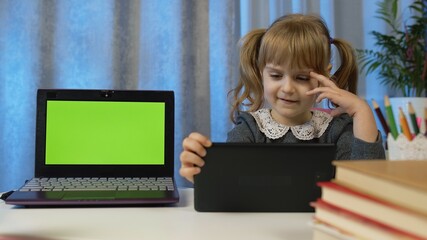 Online kids distance remote education, children e-learning lesson. Child girl pupil doing homework with teacher using digital tablet. Laptop green screen at home. Video call by webcam on internet