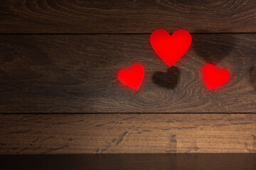 On the wooden dark background on the right frame two small and one large red heart, used as a background or postcard