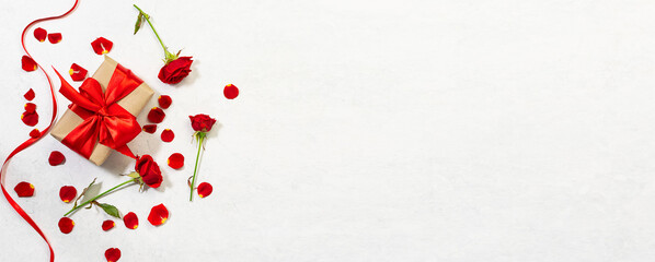 Long wide greeting banner for St. Valentine’s day with gift box, beautiful red roses and ribbon on white marble background. St. Valentine’s promo and sale banner concept.