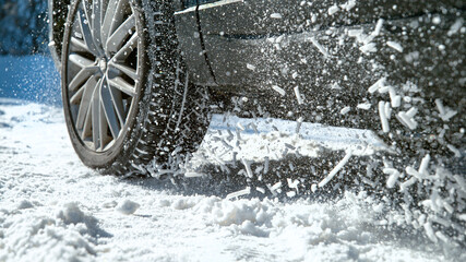 CLOSE UP: Powerful car's wheels spin in place and spew up pieces of white snow.