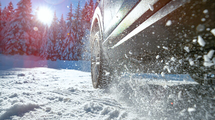 LOW ANGLE: Bright sun rays shine on car struggling to gain traction in snow.