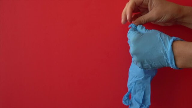 Hands Putting On Blue Gloves On The Red Background