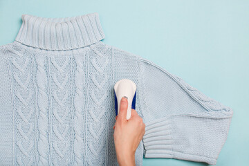 Lint Remover in woman hand on blue background. Anti-pilling razor. Device for shaving clothes. Anti-Plush fabric Shaver. Electric portable sweater pill defuzzer. Woman use Fuzz Balls Remover, top view