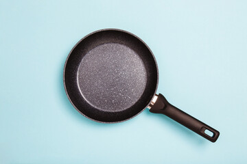 Black frying pan blue background. Simple new empty Non-stick Frying Pan with black handle isolated on blue. Top view