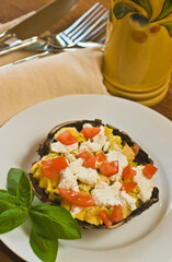 top view, close distance of a portobello mushroom cap, filled with scrambles eggs, chopped tomato and a sprig of basil in round, white bowl