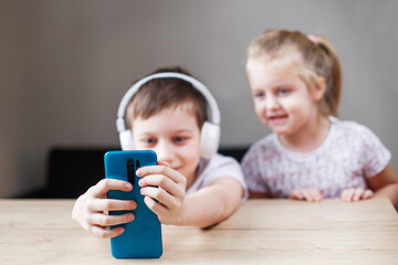 two happy children playing on the smartphone in headphones. people, children and technology concept