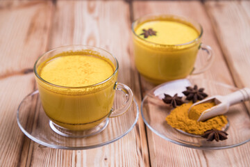Cups with Golden Milk drink and turmeric powder with wooden spoon on wooden background. Healthy antioxidant drink