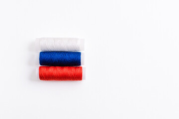 Three spools of thread for sewing are stacked in the form of the flag of Russia on a white background. Concept of Russian patriotism and the country's clothing industry. There is a free empty space.