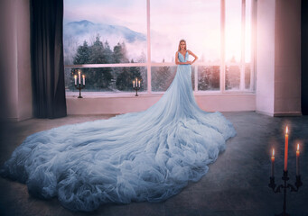 Young woman blonde fantasy princess Cinderella in glamorous blue dress stands in white room huge...