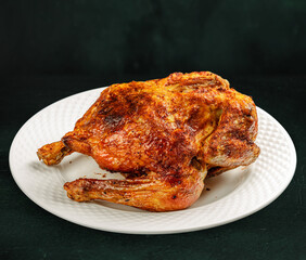 Tasty grilled fried roast chicken Tabaka in a white plate on concrete table