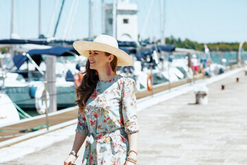 smiling trendy traveller woman in floral dress on pier