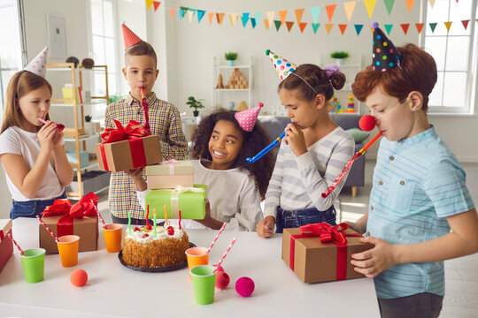 Group of smiling mixed race children in clown festive costumes with decorative whistles having birthday party and celebrating together at home. Children of different nationalities party concept