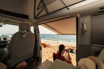 A young woman having breakfast in her caravan observing a good view of the beach