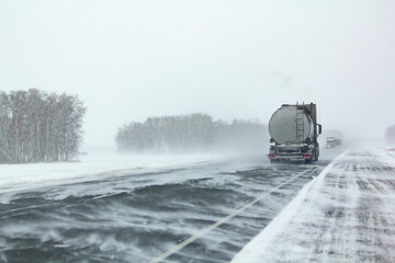 Industry vehicle moves along an asphalt road during a blizzard.