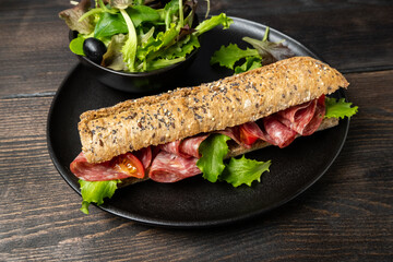 Salami sandwich with multigrain bread baguette with green lettuce and tomato. Takeaway Takeout food. Submarine sandwich top view. Healthy lunch dinner