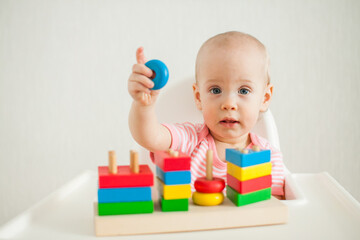 little girl plays with an educational toy - a multi-colored wooden pyramid. Development of fine motor skills and logical thinking. High quality photo