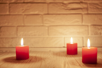 three red burning candles on a wooden background, in the background a white brick wall, used as a background