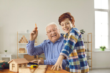 Skillful old master carpenter in retirement teaching little boy handwork skills in carpentry...