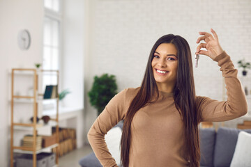 Happy woman holding keys to new home, looking at camera and smiling. Portrait of first time buyer, house owner, apartment renter, flat tenant or landlady. Moving day and buying own property concept - obrazy, fototapety, plakaty