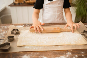 close-up of the hands of a boy cook rolling out dough on a wooden table with a rolling pin