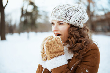 woman warming hands with breath outdoors in city park in winter