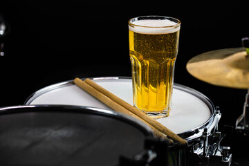 Glass of light beer on professional drum set closeup. Drumsticks, drums and cymbals, at live music...