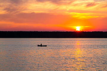 Fototapeta premium Sunset on the lake. A fisherman is fishing from a boat