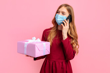 young woman in a red dress, wearing a medical mask, and talking on a cell phone, holding a gift box, on a pink background, Valentine's day concept