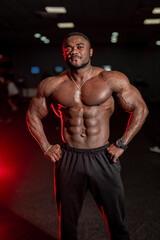 Obraz na płótnie Canvas Very muscular athlete man shows body to the camera. Perfect muscules. Dark gym background.