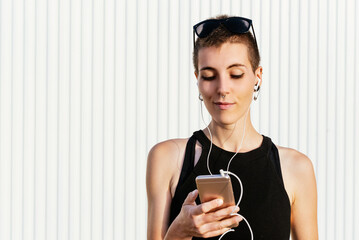 woman with short hair and piercings listening to music with headphones from her smartphone on the...