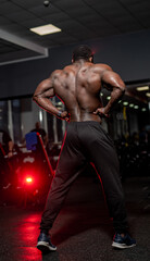 Bodybuilder african american shows strong back without shirt to the camera. Athlete poses in gym.
