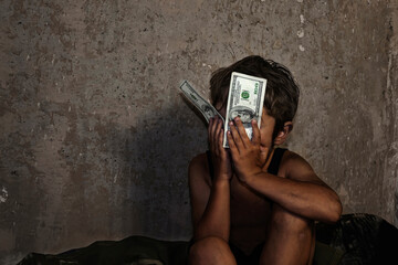 Child homeless, beggar closes his eyes with dollar bills (concept poor and rich)
