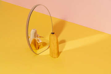 Half of banana in a mirror with one half pilled off. Dual tone background.  Creative fruit concept