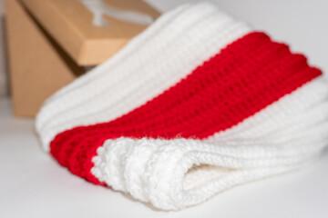 Obraz na płótnie Canvas Knitted scarf white red white neatly folded next to craft box on white background close up