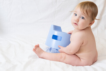 Cute blue-eyed Caucasian toddler sits near a blue nursery pot on a white background.